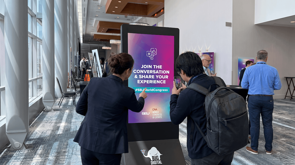 Attendees interact with a BIG Digital portable kiosk displaying social engagement content during Sports Business Journal's CAA World Congress of Sports conference.