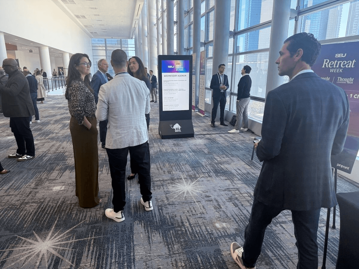 BIG Digital portable Event Network kiosk displays the conference agenda during Sports Business Journal's CAA World Congress of Sports while attendees network throughout the venue.